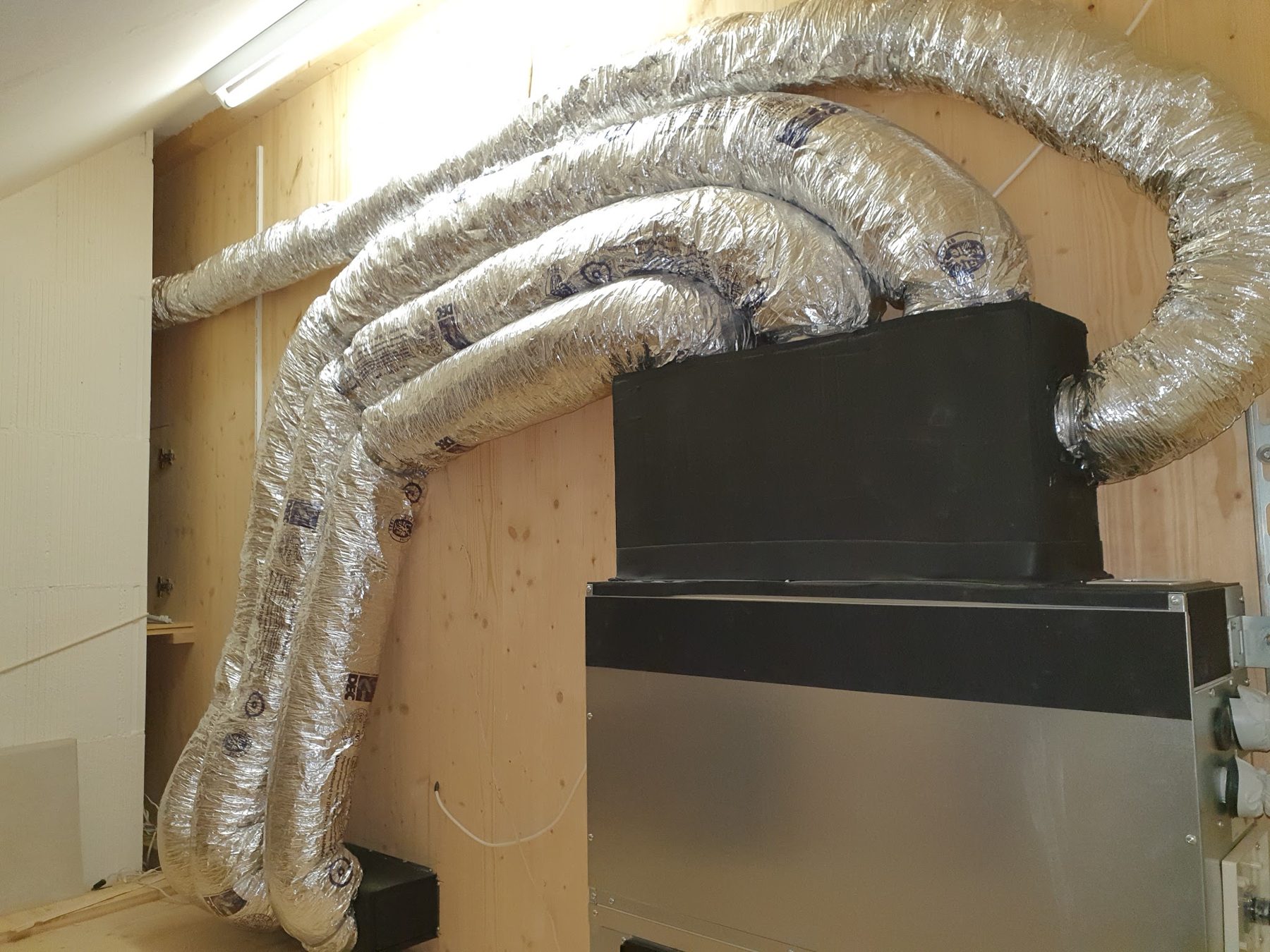 Isolierte Lüftungskanäle an einer Holzwand mit Innengerät